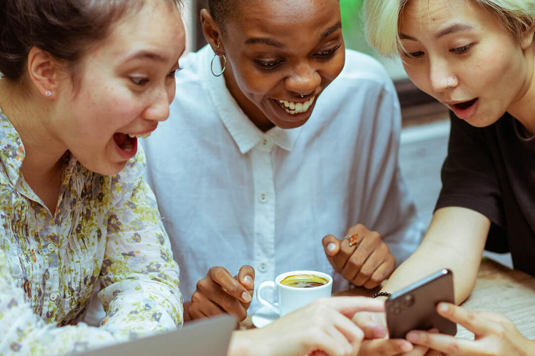 3 women looking at a mobile phone appearing surprised