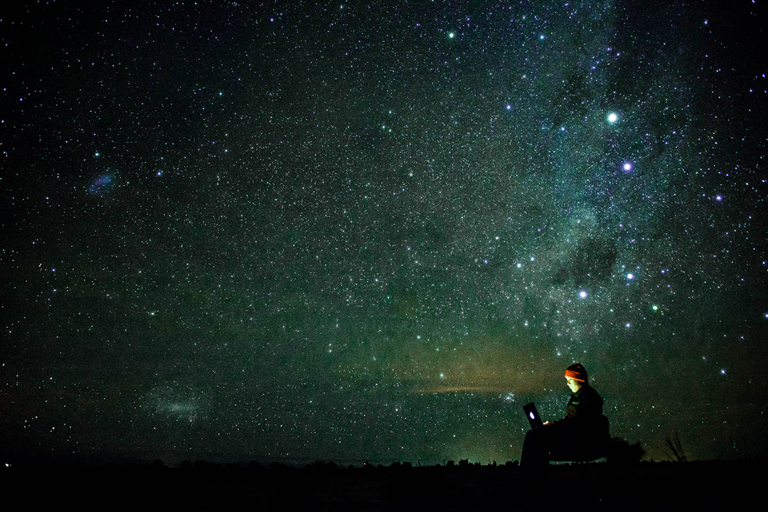 woman on laptop outdoors with the milky way night sky as background